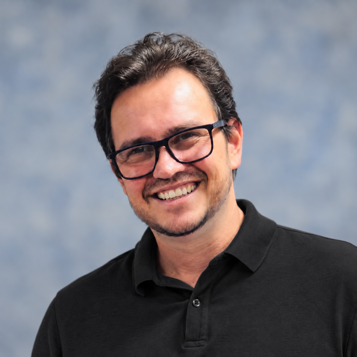 Daniel Lisbeni, sorrindo, com óculos e camisa preta.